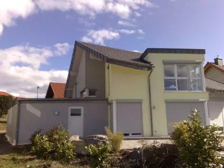 Reihenhaus mit neu eingedecktem Dach mit dunklen Dachziegeln und Garage links vom Haus in grau/violetter Farbe