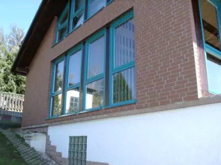 Seitenansicht einer Fassade in lehmfarbener Steinoptik mit Fenstern mit grünem Fensterrahmen