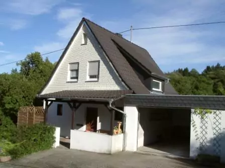 Ansicht eines Hauses mit Fassadenverkleidung in heller Steinoptik, überdachtem Eingangsbereich und Garage
